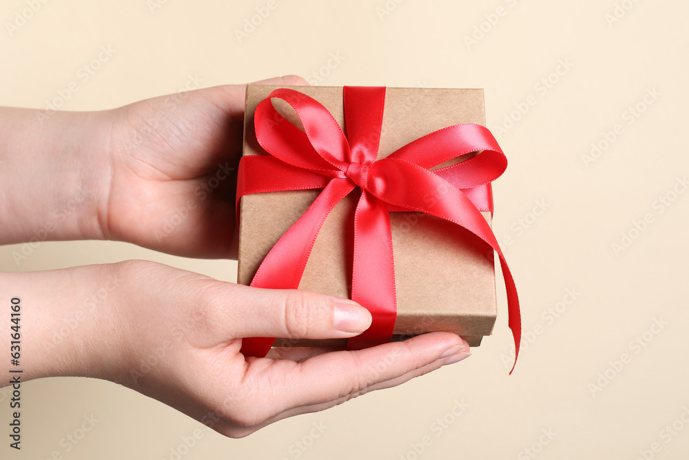 Woman holding gift box with red bow on beige background, closeup Woman holding gift box with red bow on beige background, closeup