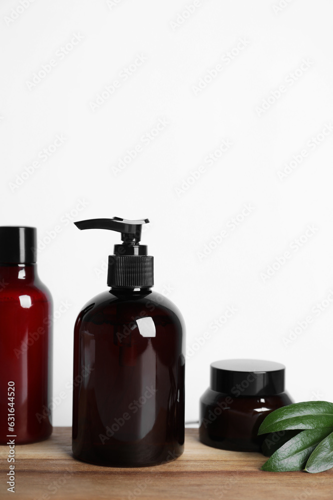 Different cosmetic products and leaves on wooden board