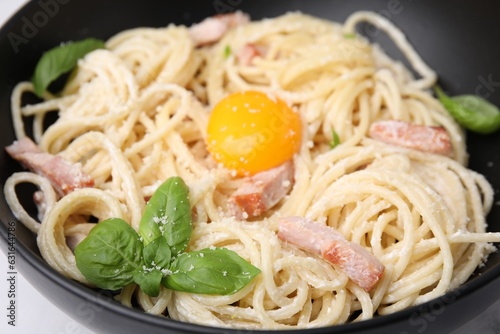 Delicious pasta Carbonara with egg yolk in black bowl, closeup