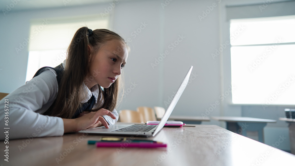 Caucasian girl sits at a desk at school and carefully looks into a laptop. Caucasian girl sits at a desk at school and carefully looks into a laptop.