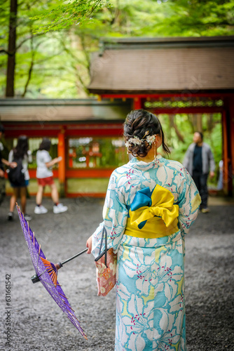 Back view of one woman wearing Japanese yukata summer kimono and holding Japanese traditional oil paper umbrella in Kifune Shrine nature forest gate, Kyoto, Japan.