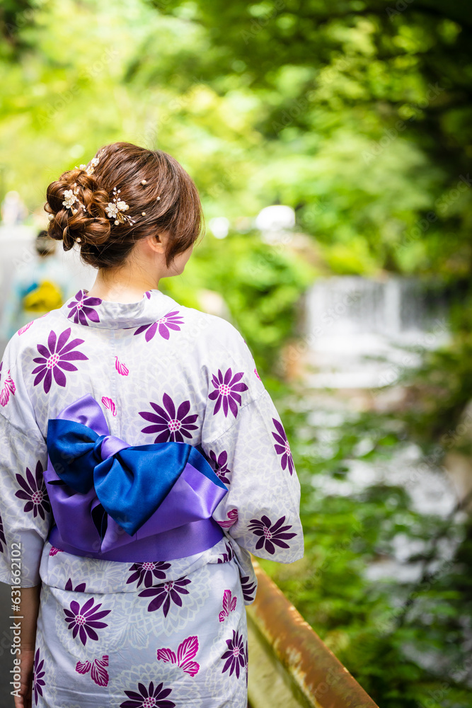 Back view of one woman wearing Japanese yukata summer kimono walking on the road next to the forest waterfall in nature. Kyoto, Japan. Back view of one woman wearing Japanese yukata summer kimono walking on the road next to the forest waterfall in nature. Kyoto, Japan.