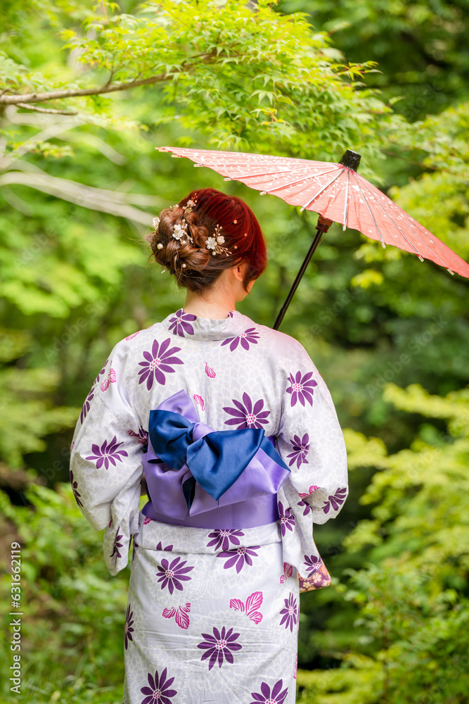 Back view of one woman wearing Japanese yukata summer kimono and holding Japanese traditional oil paper umbrella in nature forest. Kyoto, Japan. Back view of one woman wearing Japanese yukata summer kimono and holding Japanese traditional oil paper umbrella in nature forest. Kyoto, Japan.