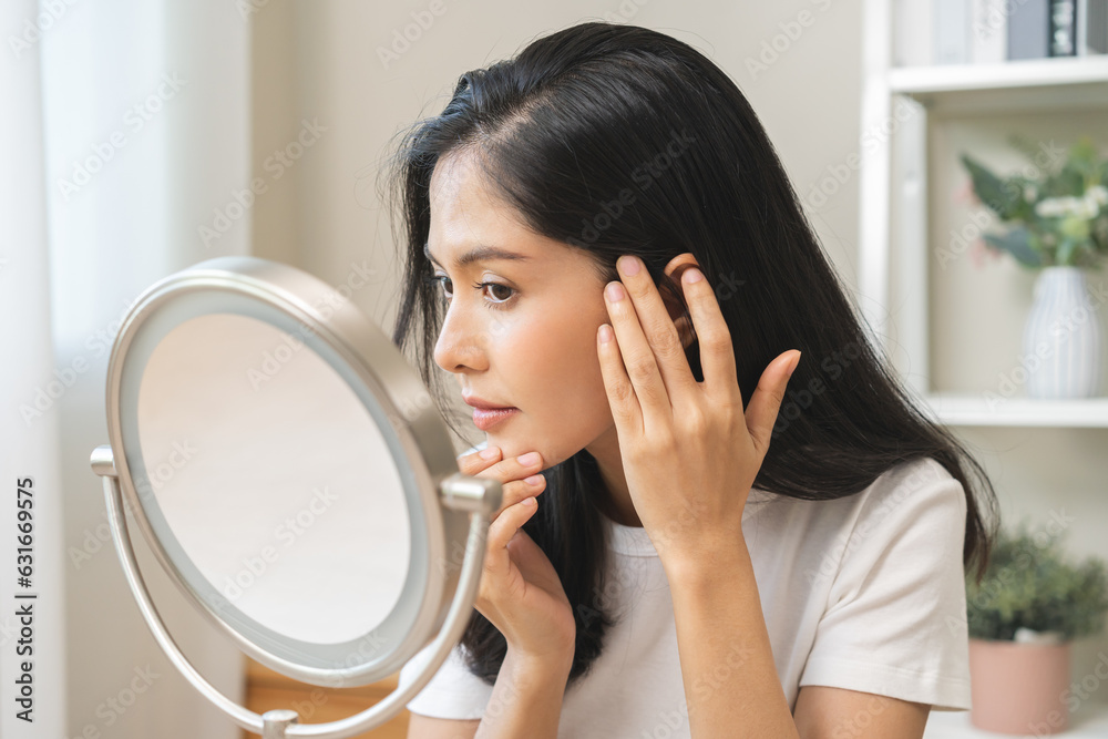 Anti aging beauty, happy asian young woman looking in mirror reflection at home, touching face skin satisfied with healthy moisturized, skin care treatment cosmetic for dry skin during morning routine Anti aging beauty, happy asian young woman looking in mirror reflection at home, touching face skin satisfied with healthy moisturized, skin care treatment cosmetic for dry skin during morning routine