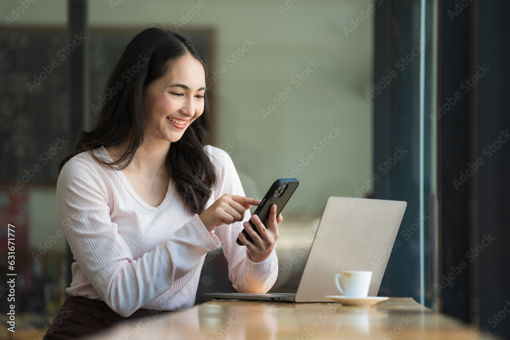 A happy young Asian woman talking on her mobile phone and smiling while sitting at her working place in a cafe.