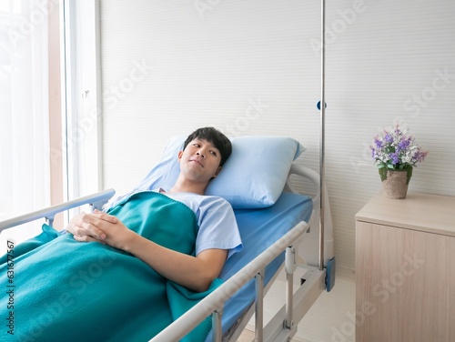 Asian happy patient man smile and healthy fine while resting in bed hospital after see doctor, nurse and visitor encouraged him at the door room