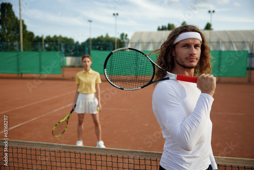 Couple of friends playing tennis on court with focus on confident man © Nomad_Soul