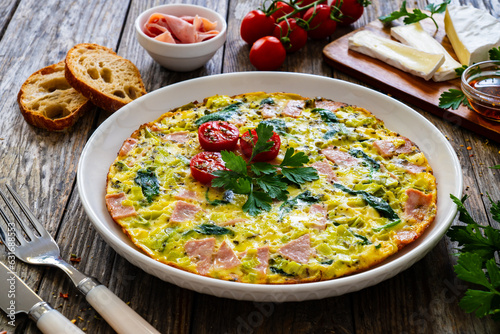 Delicious breakfast - egg omelette with mortadella, leek,spinach and cherry tomatoes on wooden table 