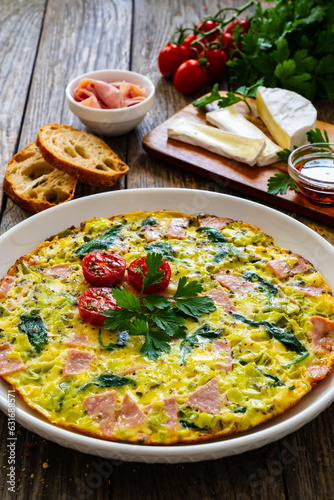 Delicious breakfast - egg omelette with mortadella, leek,spinach and cherry tomatoes on wooden table 