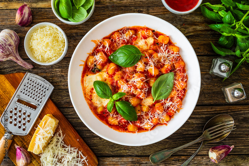 Gnocchi alla sorrentina - gnocchi with melted mozzarella cheese in tomato sauce and  Parmigiano Reggiano on wooden table
