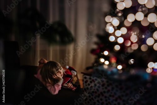 girl watching tv and cuddling her elf in front of the christmas tree photo