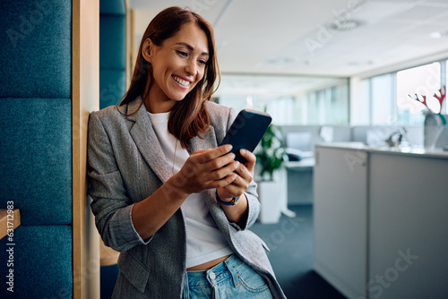 Happy female entrepreneur using smart phone in office. photo