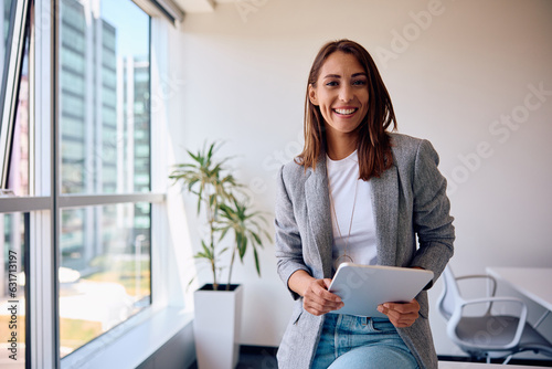 Young happy businesswoman using touchpad while working in office and looking at camera.