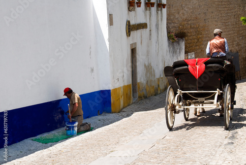 Obidos, Portugal, Europe - UNESCO World Heritage Site, street scene, man renewing paints on the wall with symbolic Portuguese colors - white, blue and yellow, horse drawn carriage passing by