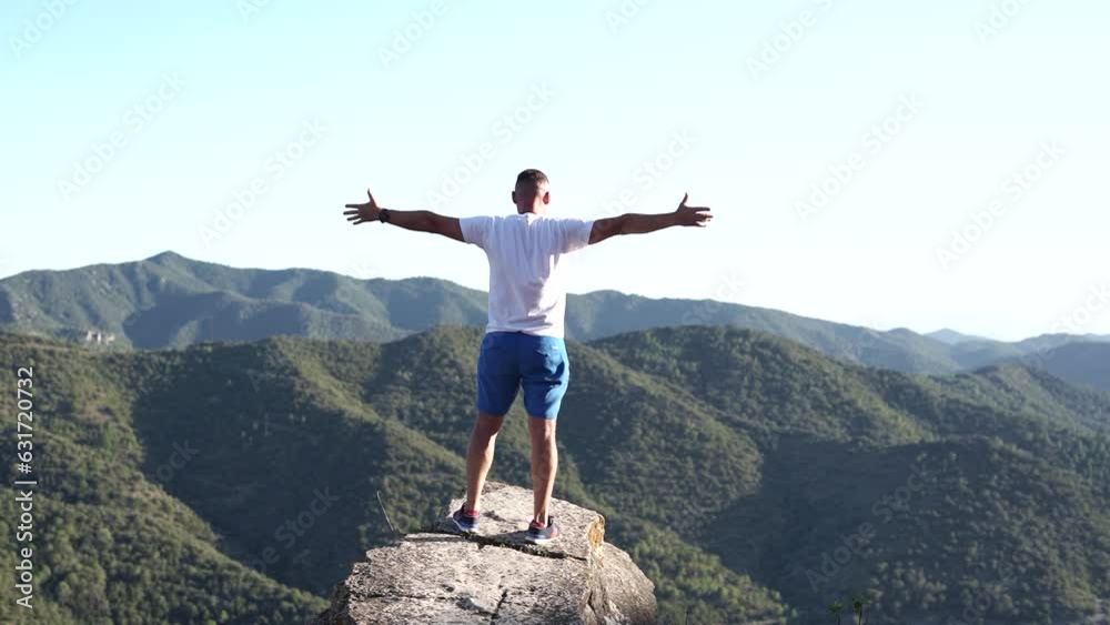 Tourist man on top of high rocks stands spread his arms. Feelings of freedom and achievement. Tourist man on top of high rocks stands spread his arms. Feelings of freedom and achievement.