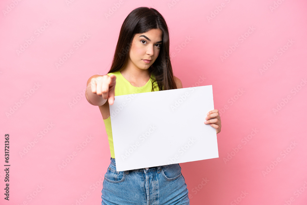 Young Brazilian woman isolated on pink background holding an empty placard and pointing to the front Young Brazilian woman isolated on pink background holding an empty placard and pointing to the front