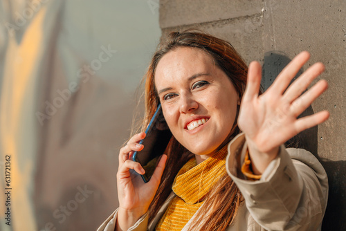 young woman using smartphone and waving in the street