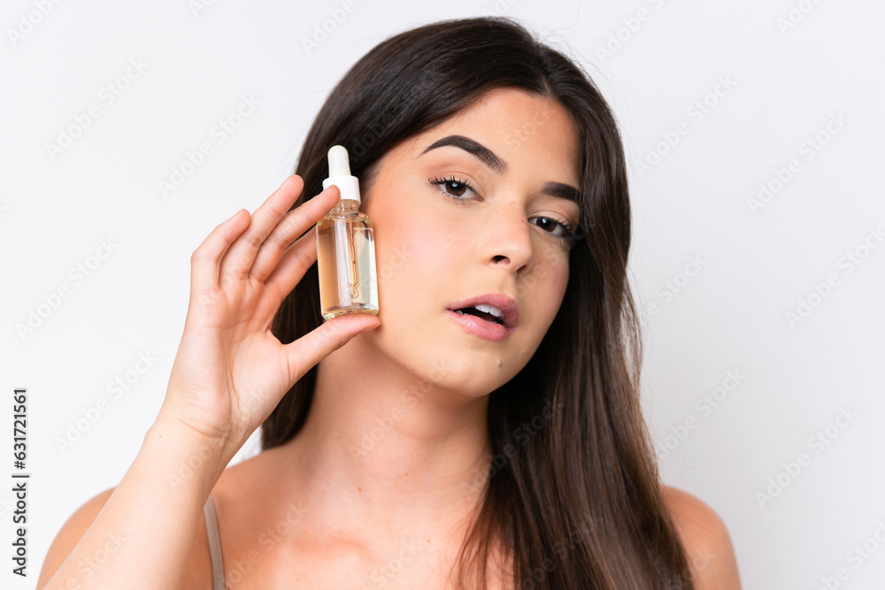 Young Brazilian woman isolated on white background holding a serum while smiling. Close up portrait