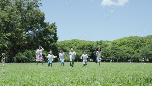 緑地でかけっこをする子供たちと、見守る女性