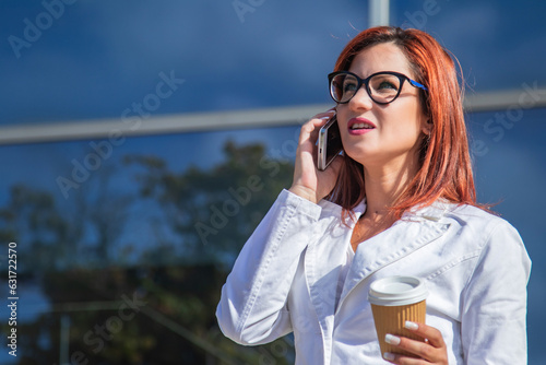 business woman drinking a coffee and talking on the mobile phone with offices in the background