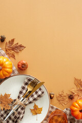 Fall-themed table setup idea. Top view vertical shot of plate, cutlery, checkered napkin, tablecloth, glass, pumpkins, anise, acorns, maple leaves on pastel brown background with space for ad or text