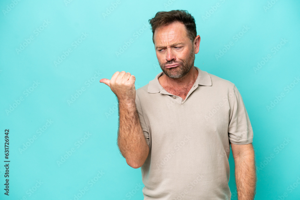 Middle age caucasian man isolated on blue background unhappy and pointing to the side Middle age caucasian man isolated on blue background unhappy and pointing to the side