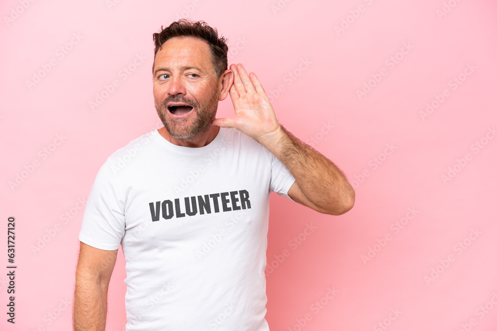 Middle age volunteer man isolated on pink background isolated on pink background listening to something by putting hand on the ear Middle age volunteer man isolated on pink background isolated on pink background listening to something by putting hand on the ear