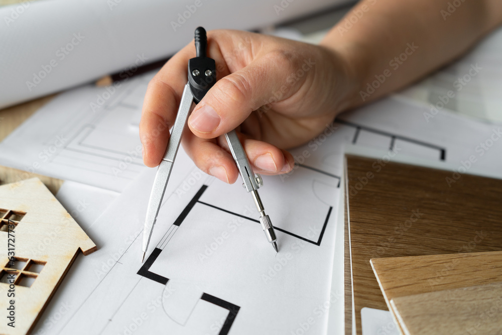 Female architect or interior designer holding compass drawing tool. Woman working on home floor plans. Building structural blueprint projects on the table. Design studio desk scene. Female architect or interior designer holding compass drawing tool. Woman working on home floor plans. Building structural blueprint projects on the table. Design studio desk scene.