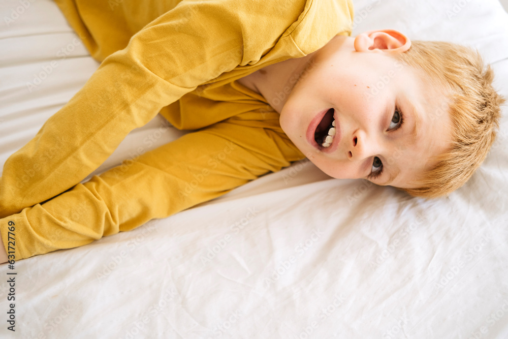 Obraz premium A playful red-haired boy finds comfort and joy on a pure white bed, a portrait of youthful energy