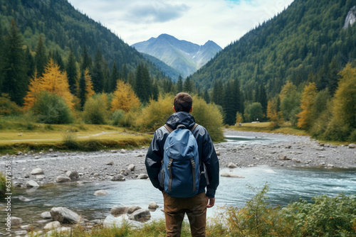 Unrecognizable adult with a blue backpack travels along the mouth of a mountain river against the backdrop of a wild forest, Rear View © alisaaa