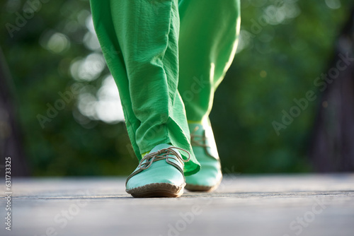 A woman in green trousers and moccasins walks along the road in summer photo