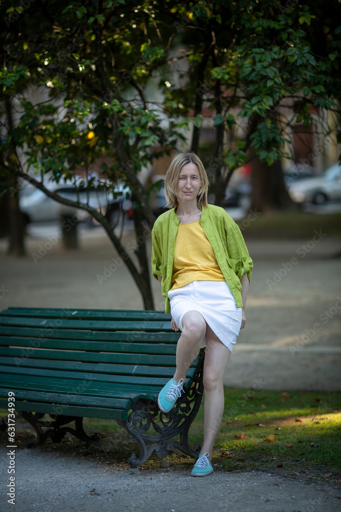 A woman in a skirt sits on a park bench.