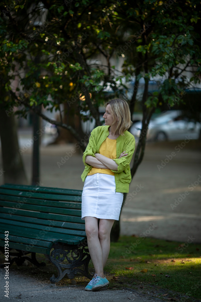 A woman sits waiting for her prince on a bench in a city park.