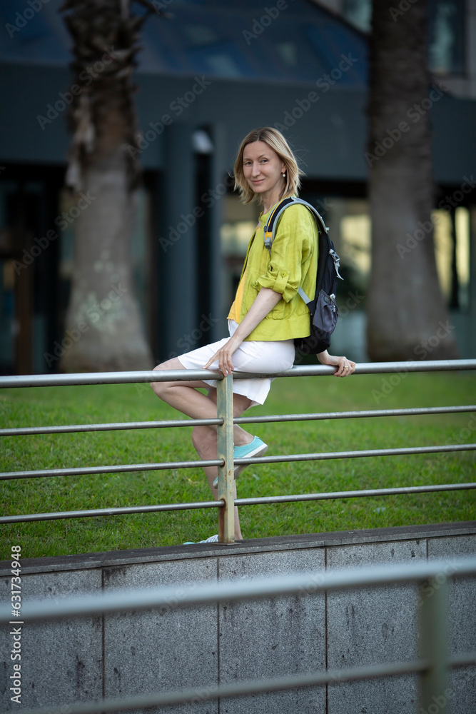A woman in a white skirt sits on the railing near the crosswalk.