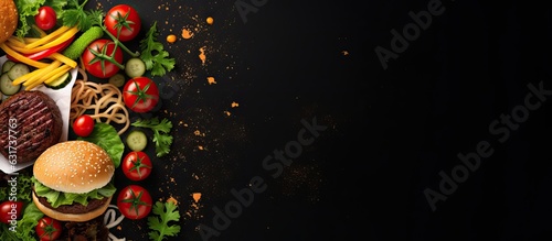The idea of fast food and unhealthy food is represented by a tasty grilled burger featuring beef, tomatoes, cheese, cucumber, and lettuce, placed on a dark background. This top view image provides