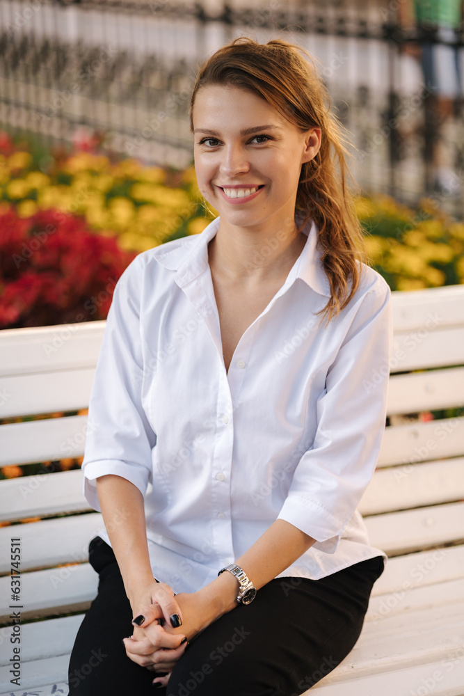 Portrait of attractive young lady in forma outfit sitting on bench in centre of city.