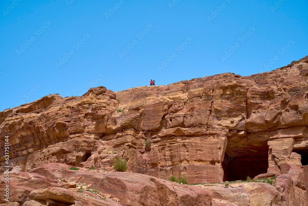 Two tourists overlooking the ruins while on a day-trip though the city of Petra, Jordan