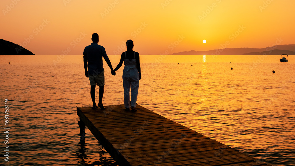a couple of men and women on a wooden jetty, looking at colorful sunset on the sea, men, and women watching a sunset in Crete Greece Europe on a wooden pier in the ocean