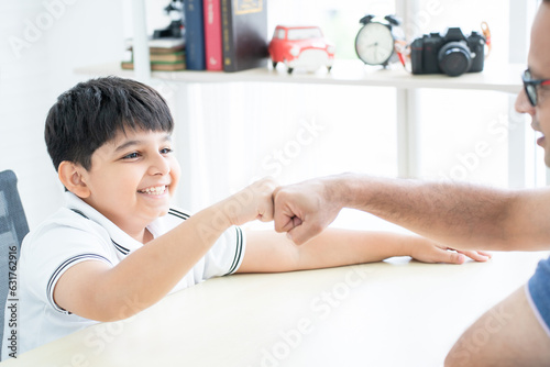 Little handsome Indian child son and his father  doing fist bump  smiling  looking at each other while dealing something together at home. Family relationship  Activity Concept