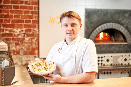 The chef holds a pizza in his hands. Neapolitan pizza from a wood-fired oven. Pizza is on the plate. Pizza with pear and gorgonzola. Fast delivery of food. 