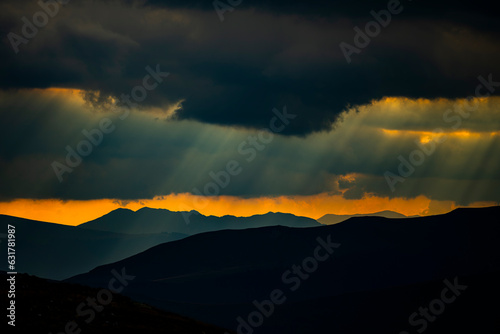 Dark mountain background. Dramatic sky with the rays of the setting sun. Retezat-Godeanu mountains, Romania.