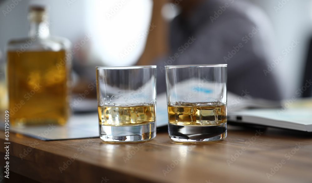 Close-up of two glassful with strong drink on wooden table. Colleagues relaxing after busy day. Employee celebrating signing contract. Business concept Close-up of two glassful with strong drink on wooden table. Colleagues relaxing after busy day. Employee celebrating signing contract. Business concept