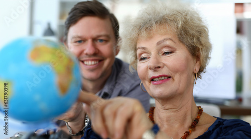Portrait of aged mother pointing at coloured globe and smiling. Cheerful adult son helping female to choose country to travel. Travelling together concept