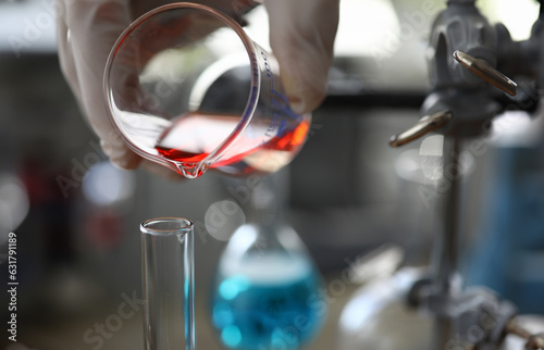 Close-up of assistant hand holding flask. Chemist pouring red liquid into vial. Researcher making mixture of fluid for experiment in lab. Chemical experiments concept