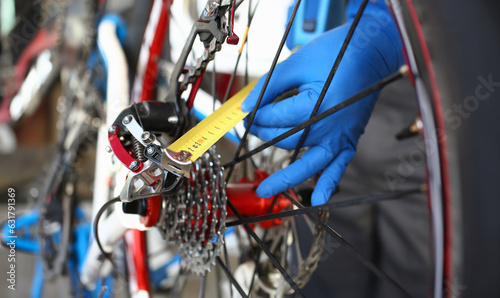 Close-up of male hands using measure tape for problem identification. Skilled mechanic working in bicycle repair shop service. Technical expertise concept