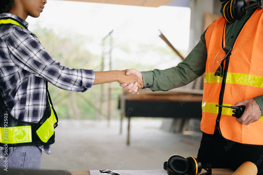 Construction team shake hands greeting start new project plan behind yellow helmet on desk in office center to consults about their building project.. Construction team shake hands greeting start new project plan behind yellow helmet on desk in office center to consults about their building project..