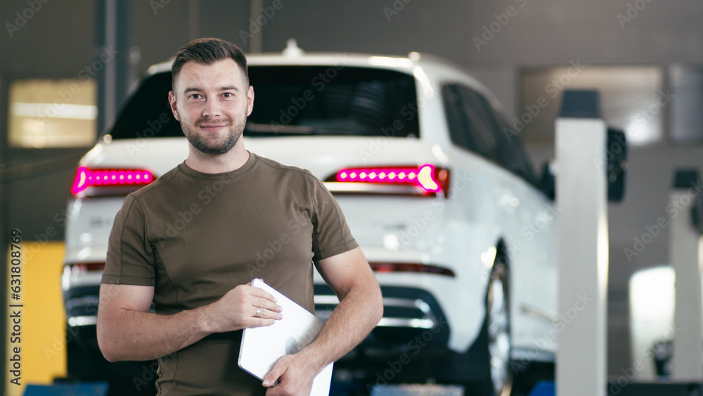 
Portrait of a handsome young male, a car salesman in a suit, posing at a workplace in a car dealership, a young dealership manager with a clipboard in his hands.