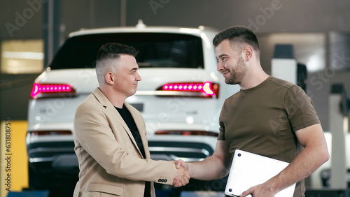 service station, a young professional man shows a satisfied client on a tablet the technical condition of the car, smiles and gives the keys to the car © Vladislav