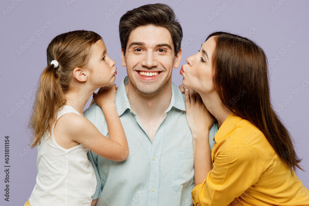 Close up young smiling happy parents mom dad with child kid daughter girl 6 years old wear blue yellow casual clothes try to kiss father husband isolated on plain purple background Family day concept Close up young smiling happy parents mom dad with child kid daughter girl 6 years old wear blue yellow casual clothes try to kiss father husband isolated on plain purple background Family day concept