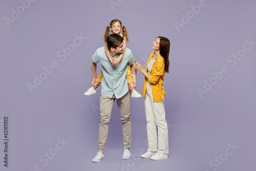 Full body young smiling happy parents mom dad with child kid daughter girl 6 years old wear blue yellow casual clothes giving piggyback ride to joyful, sit on back isolated on plain purple background.